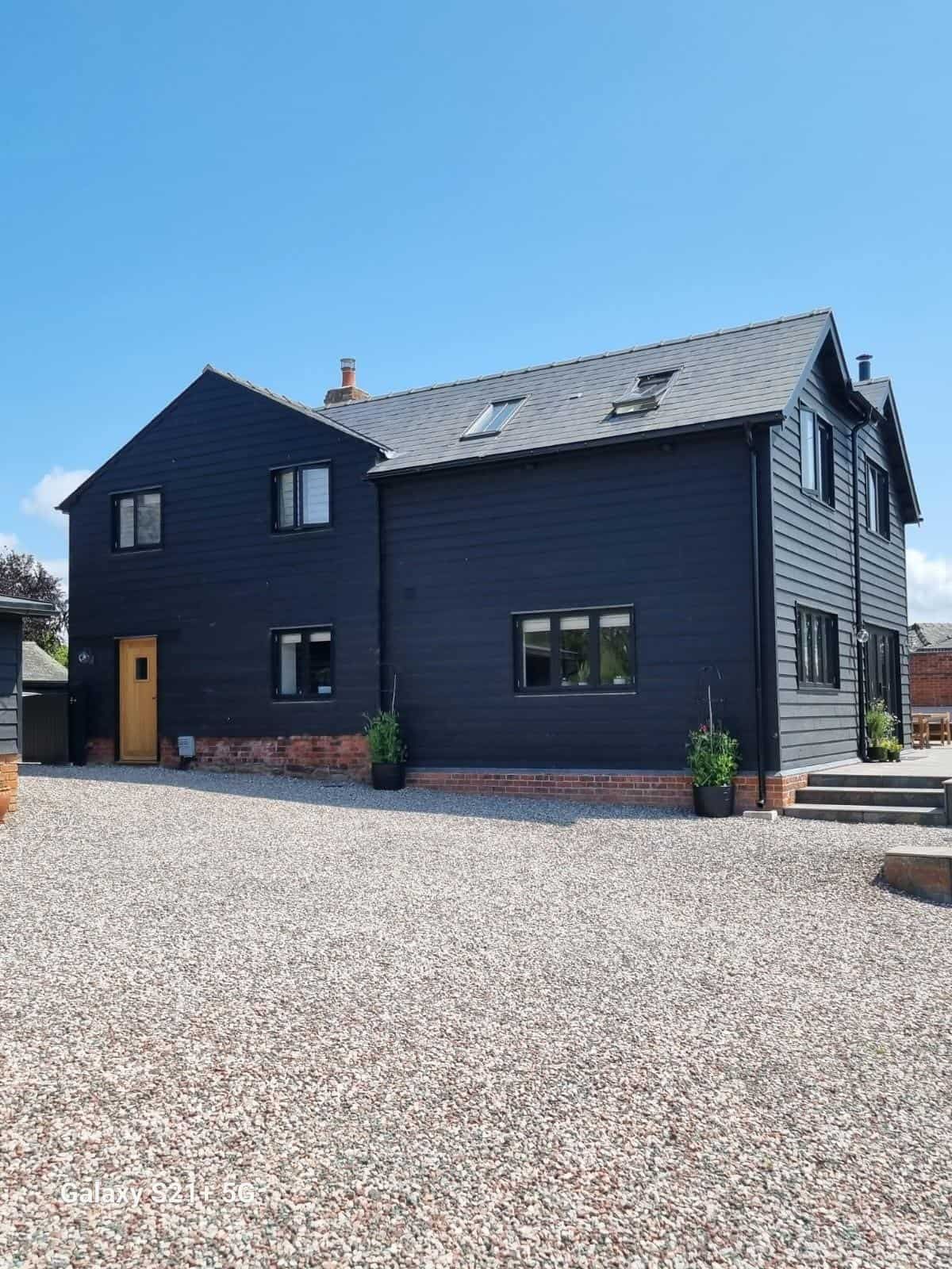 Converted barn with black weatherboarding and gravel drive